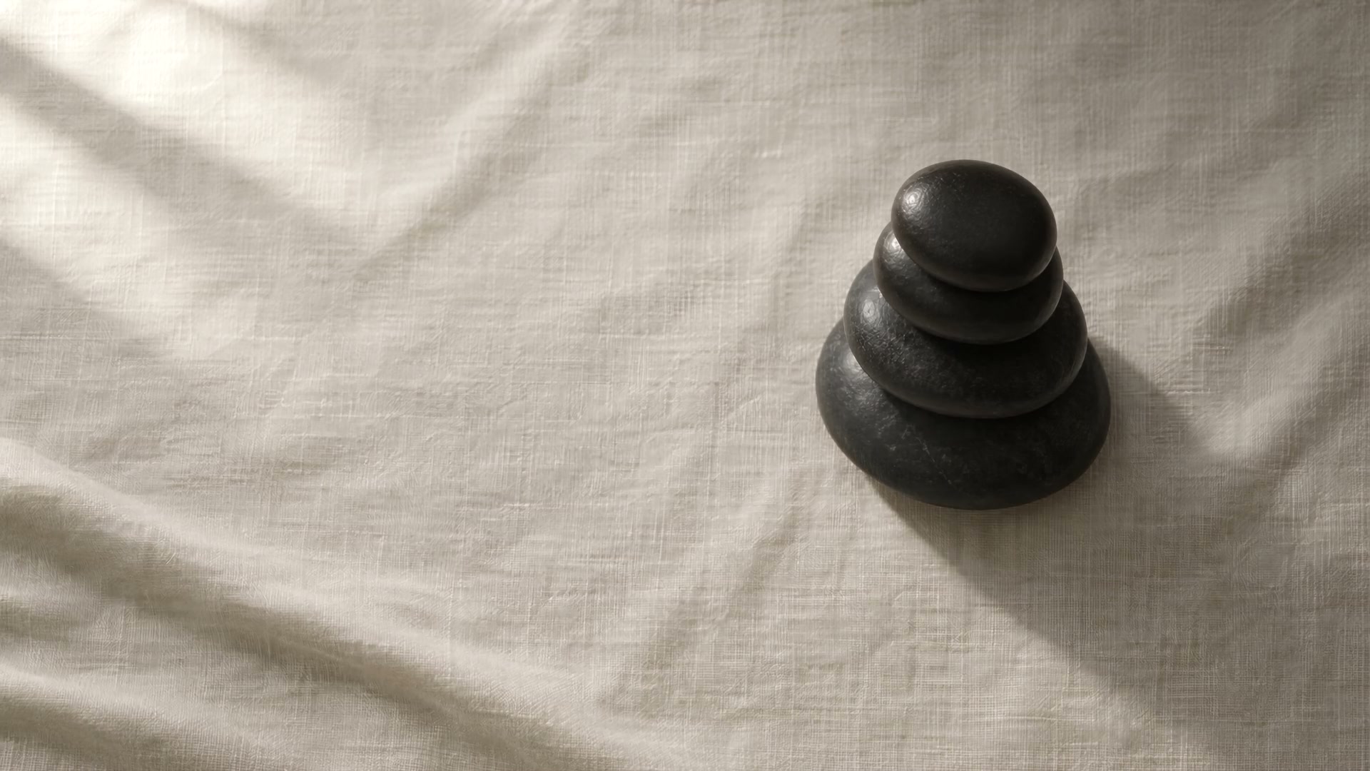 Four black massage stones balanced on white linen